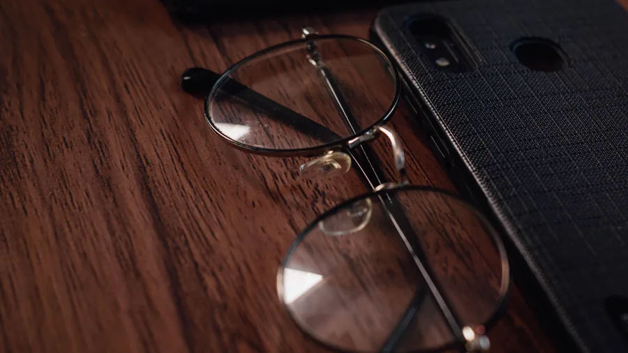 Een bril met dun montuur ligt naast een smartphone op een donkere houten tafel