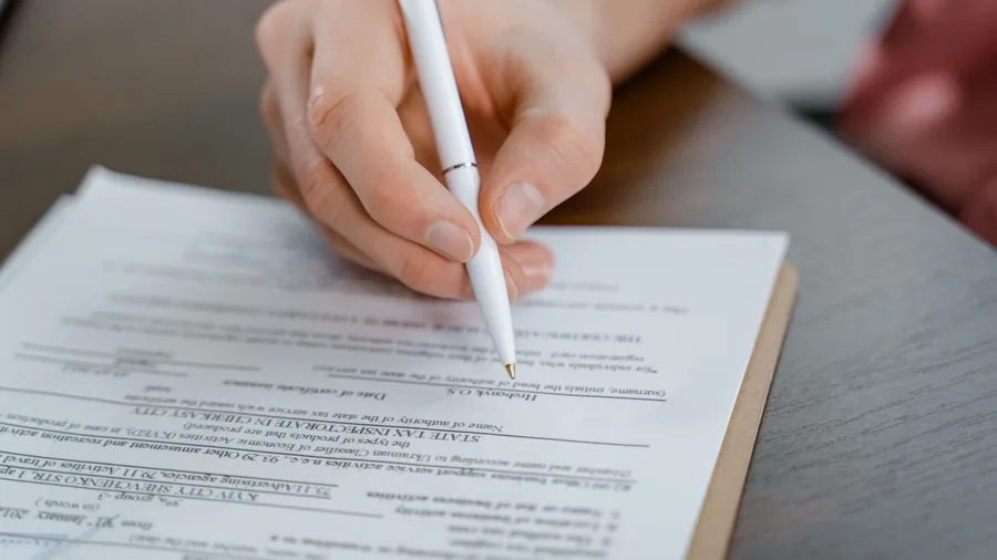 Een hand met een witte pen zet een handtekening op een bedrukt formulier