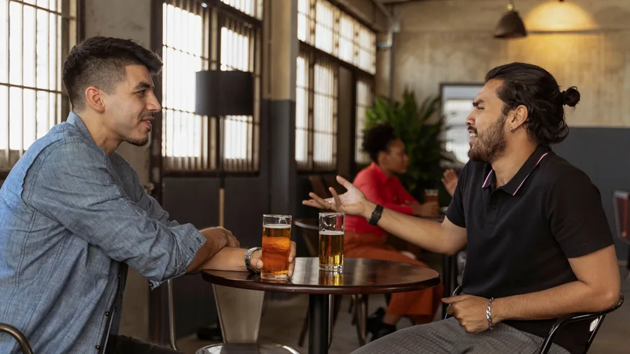 Twee mannen zitten aan een rond tafeltje in een cafe en praten met elkaar