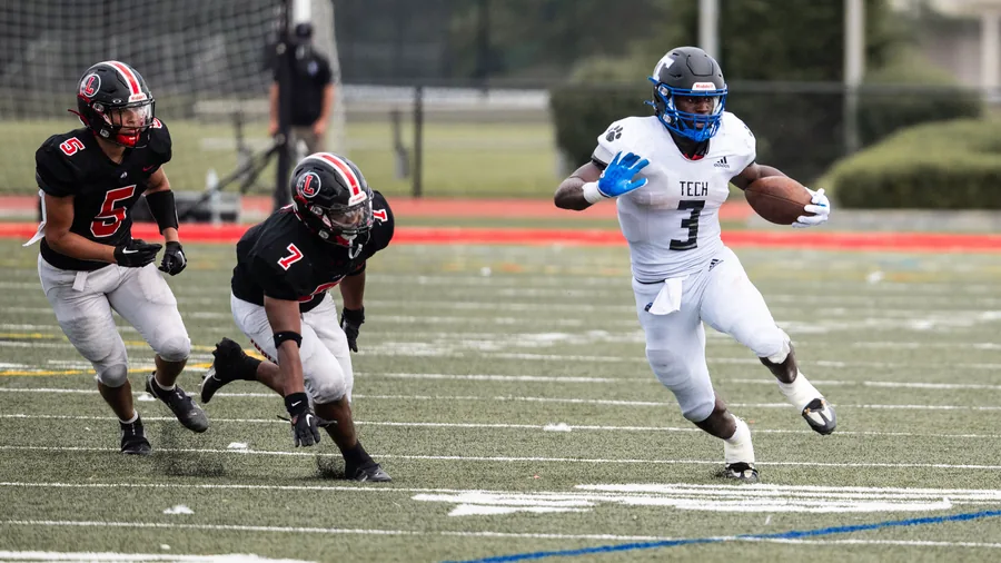 Speler in wit tenue rent met de bal langs twee verdedigers in het zwart tijdens een wedstrijd American football
