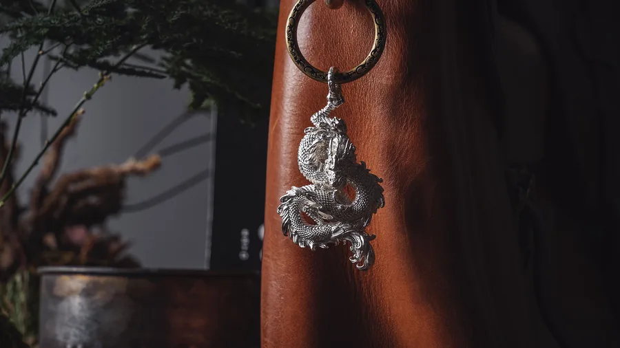 Zilveren sleutelhanger in de vorm van een draak hangt aan een bruine leren tas
