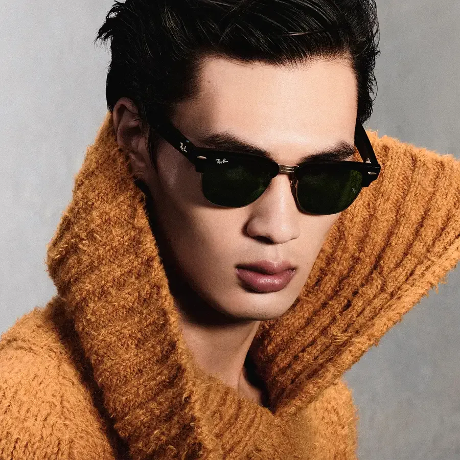 Man in een oranje trui met de Ray-Ban Meta Audio Clubmaster met groene zonneglazen