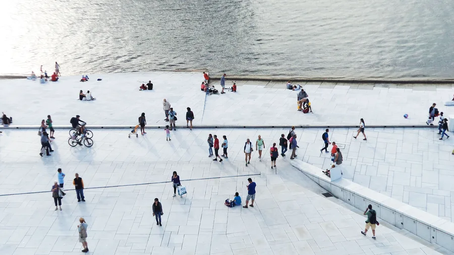 Tientallen mensen lopen en zitten verspreid over een wit plein aan het water