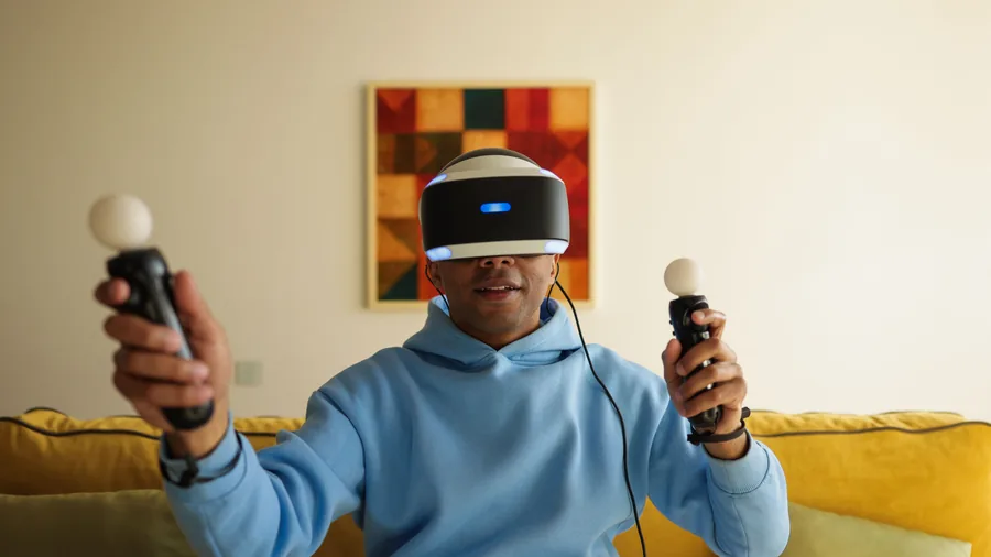 Speler op een gele bank met een PlayStation VR-bril op en een bewegingscontroller in elke hand