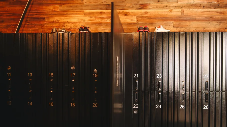 Rij donkere genummerde kluisjes onder een houten wand in de kleedkamer van een sportclub