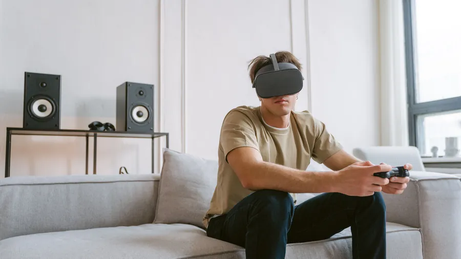 Man met een grijze VR bril en een gamecontroller zit op de bank in een lichte woonkamer