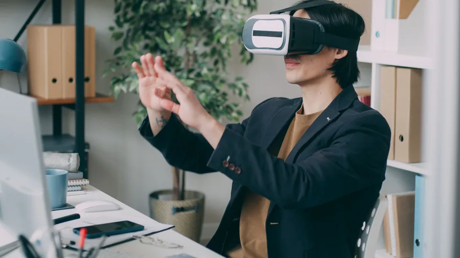 Man met een VR bril op achter zijn bureau met de computer binnen handbereik