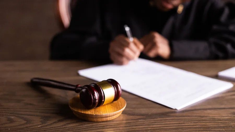 Iemand in een zwarte toga ondertekent een document naast een houten rechtershamer op tafel