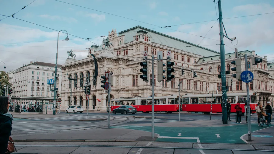 Een rode tram rijdt langs de Weense Staatsopera op een kruispunt met verkeerslichten