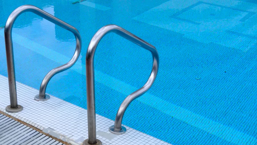 Een roestvrijstalen trap in een binnenzwembad met helderblauw water en witte tegels